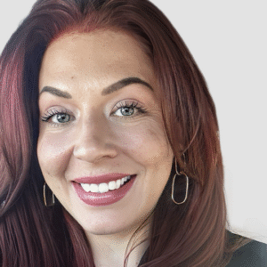 A woman with long red hair, blue eyes, and hoop earrings smiles brightly in a close-up portrait.