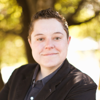 Censys Alexis with short dark hair, wearing a black jacket and smiling outdoors in sunlight.