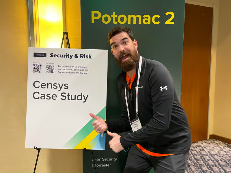 Man pointing at a "Censys Case Study" sign at a security event, standing in front of a Potomac 2 sign.