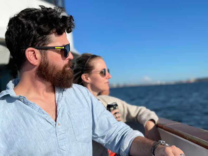 Three people with sunglasses relax on a boat against a blue sky and water background.