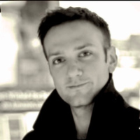 A young man with short hair and a slight smile, wearing a dark jacket, in a black-and-white portrait.
