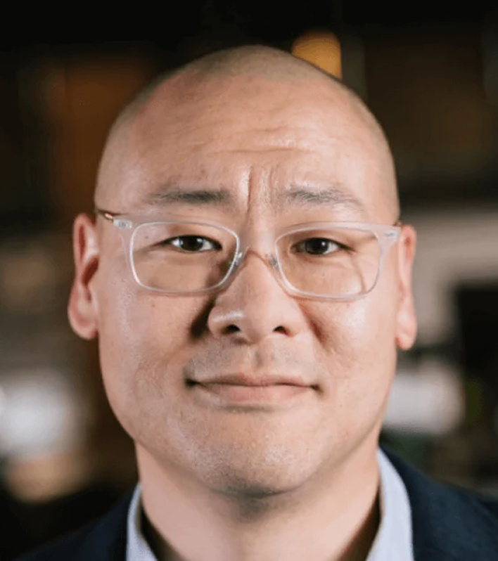 Dug Song, a leader at Censys, with a shaved head, glasses, and a calm expression, in a professional setting.