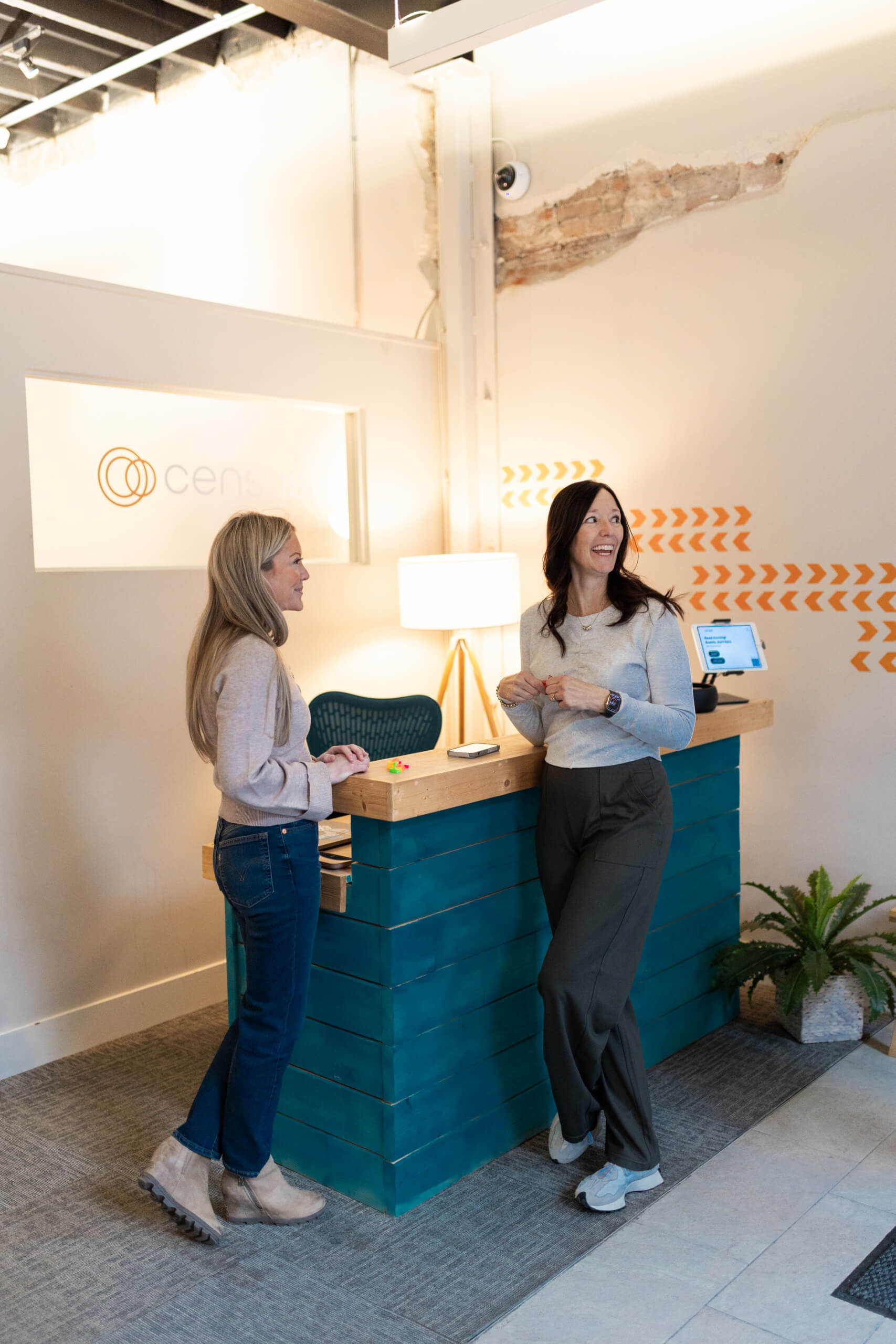 Two women laughing and chatting by a teal front desk in the Censys office lobby with branded signage.