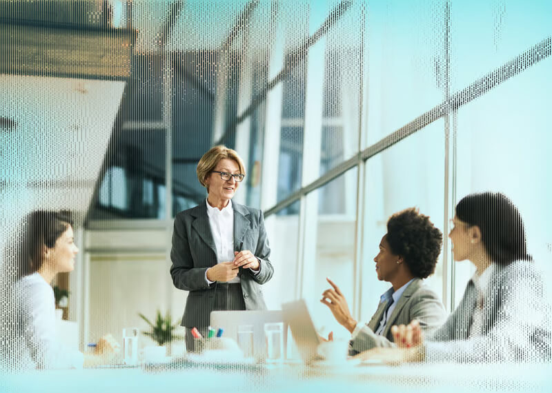Censys Our Customers Hero A professional woman presents to a diverse group of colleagues in a modern office setting during a meeting.