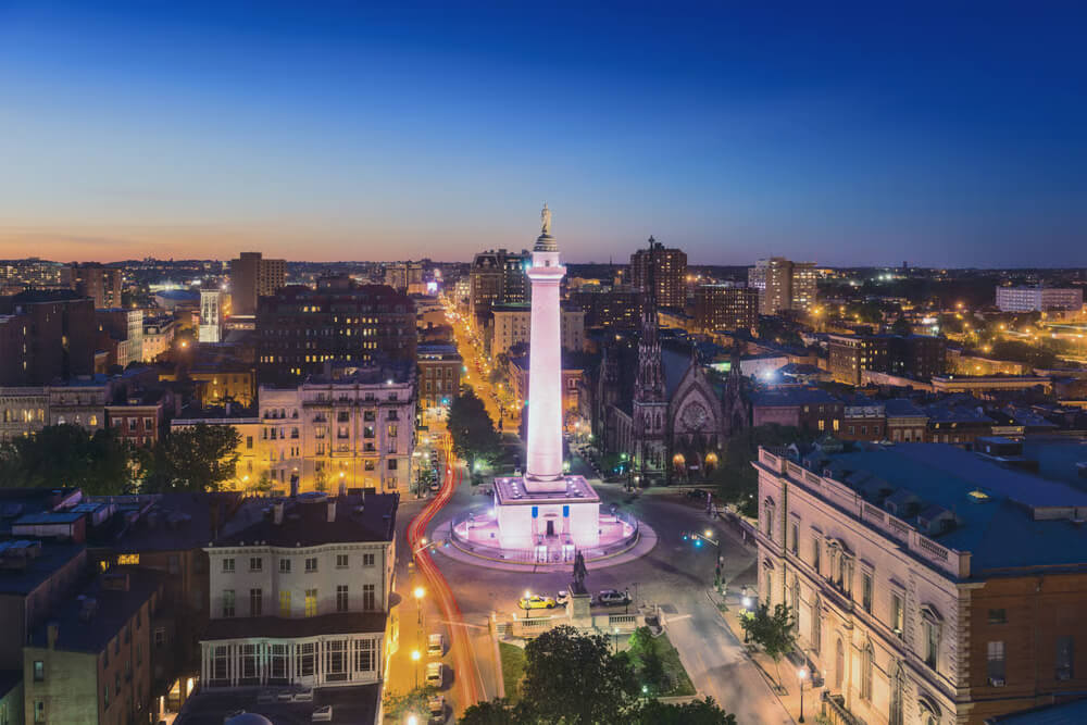 Aerial view of a cityscape at dusk with a lit-up monument in the center and illuminated buildings and streets.