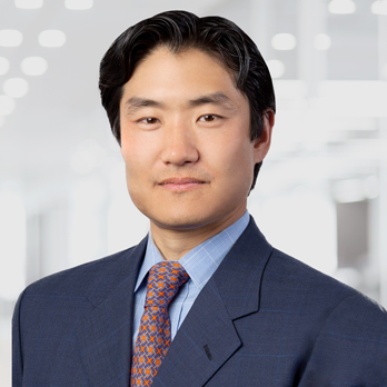 Pete Chung, a man with dark hair wearing a navy suit, light blue shirt, and orange patterned tie, poses for a headshot.